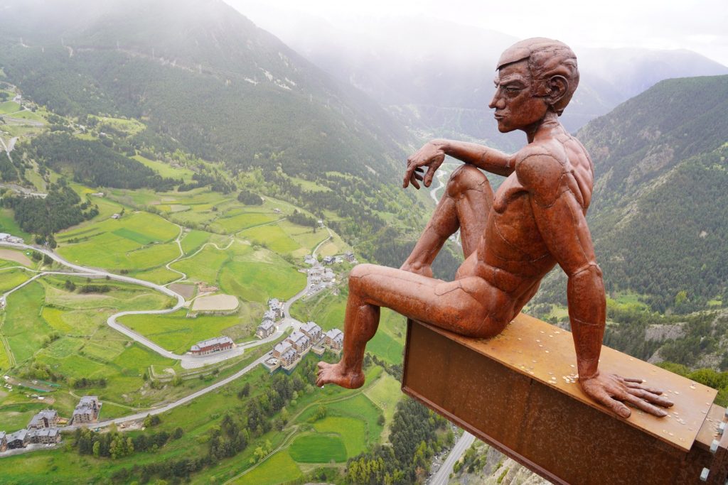 Statue von einem Mann der auf einem Stahlträger über einem Abgrund sitzt und eine tolle Aussicht ins Tal hat.